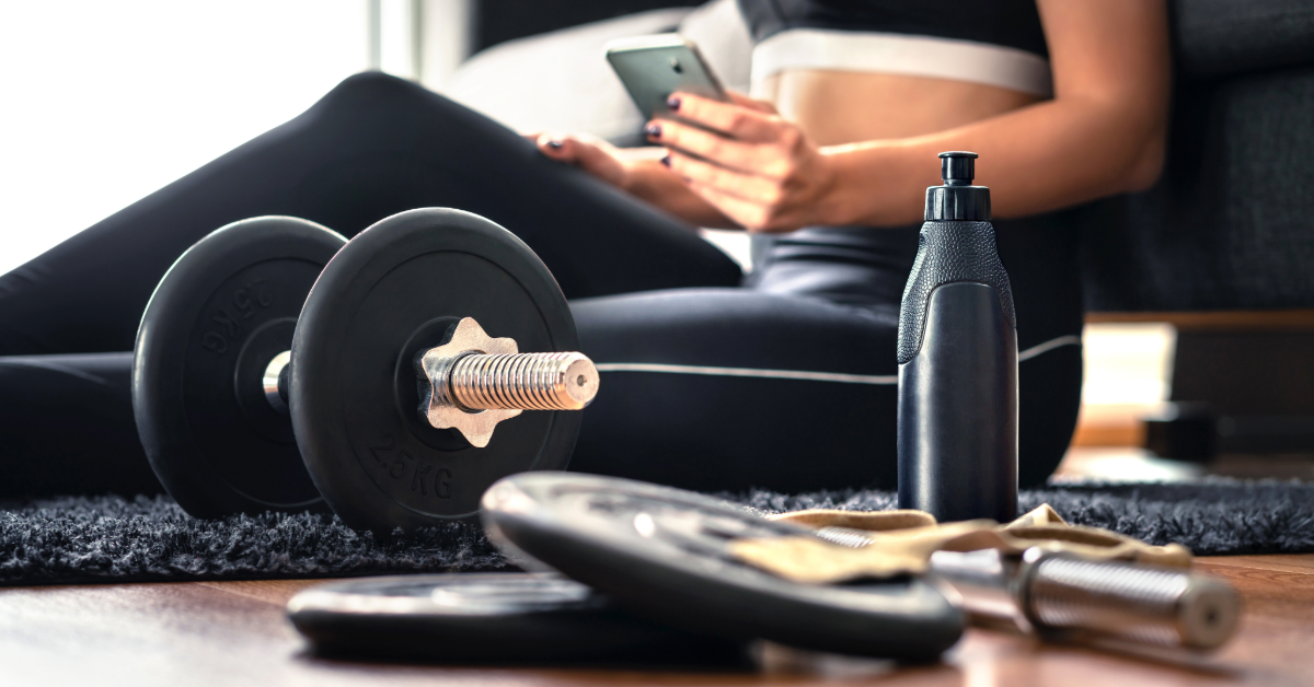 A woman checking her home workout plan from Renew Wellness with a variety of home workout equipment around her