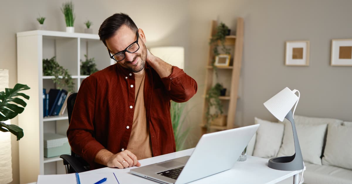 Middle aged man at his desk grabbing neck in pain from looking down at laptop computer too long
